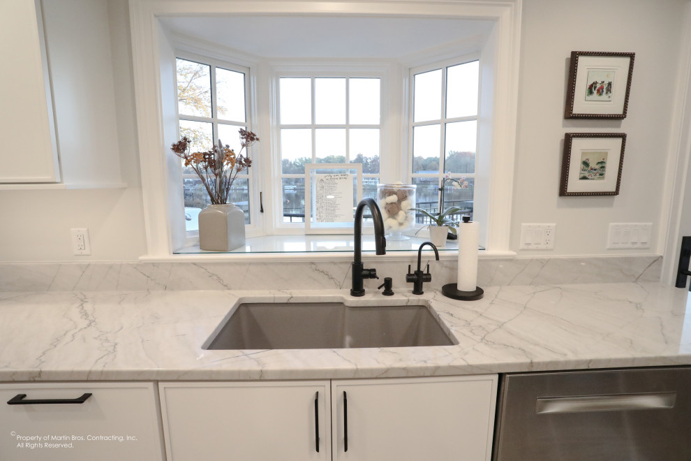 Example of a large transitional u-shaped light wood floor open concept kitchen design with an undermount sink, flat-panel cabinets, white cabinets, quartzite countertops, white backsplash, porcelain backsplash, stainless steel appliances, an island and white countertops