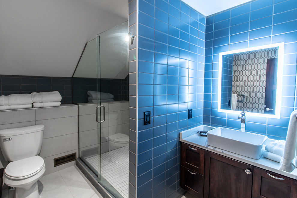 Inspiration for a mid-sized transitional 3/4 blue tile and ceramic tile ceramic tile and gray floor alcove shower remodel with shaker cabinets, dark wood cabinets, a two-piece toilet, gray walls, a vessel sink, quartz countertops, a hinged shower door and white countertops