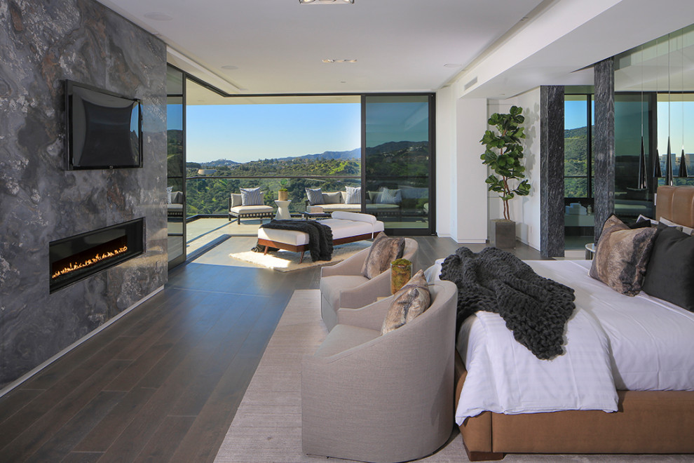 Large modern master bedroom in Los Angeles with white walls, dark hardwood floors, a ribbon fireplace, a stone fireplace surround and grey floor.
