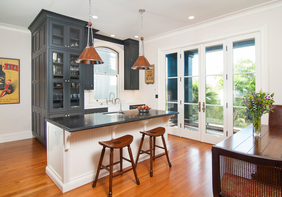 This is an example of a mid-sized traditional separate kitchen in San Francisco with a farmhouse sink, recessed-panel cabinets, black cabinets, marble benchtops, white splashback, subway tile splashback, panelled appliances, light hardwood floors and with island.