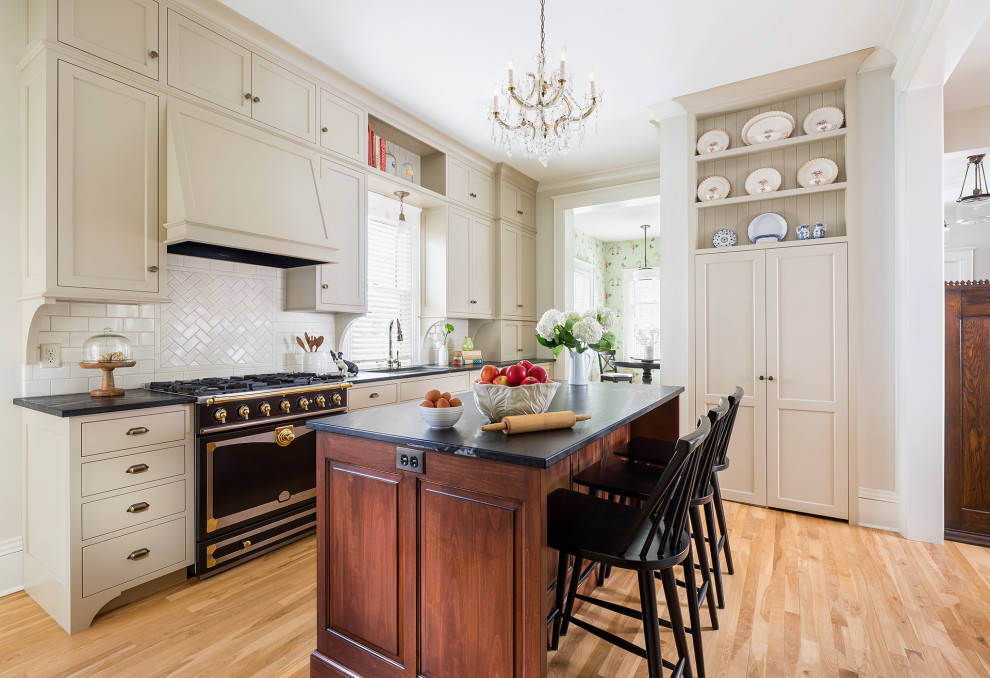 Inspiration for a large transitional single-wall separate kitchen in Minneapolis with an undermount sink, flat-panel cabinets, beige cabinets, soapstone benchtops, white splashback, ceramic splashback, black appliances, medium hardwood floors, with island, brown floor and black benchtop.