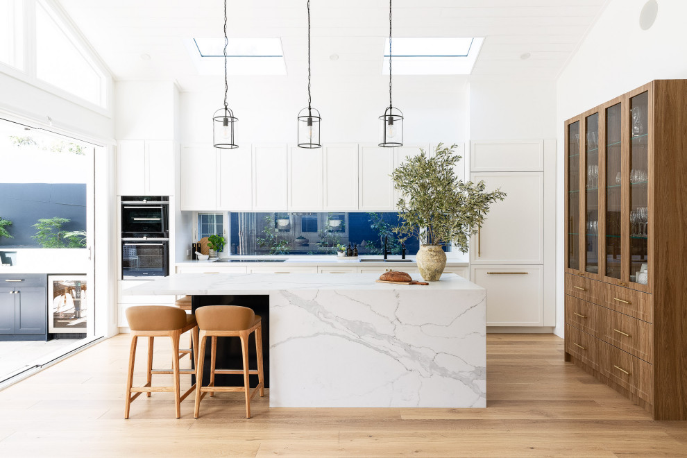 Inspiration for a large beach style galley kitchen in Sydney with shaker cabinets, white cabinets, marble benchtops, with island, white benchtop, vaulted, timber, window splashback, panelled appliances, medium hardwood floors and brown floor.