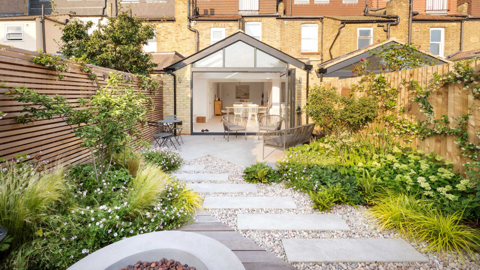 This is an example of a small contemporary back garden in London with a fire feature, decorative stones and a wood fence.