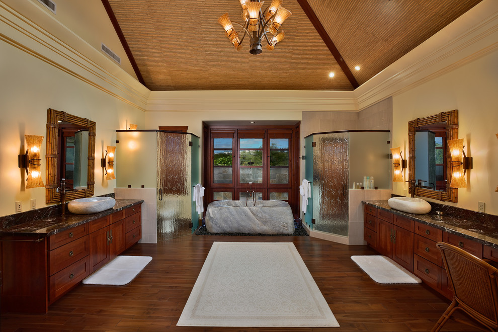 Photo of a large asian master bathroom in Hawaii with a vessel sink, shaker cabinets, medium wood cabinets, a freestanding tub, a corner shower, marble benchtops, yellow walls and medium hardwood floors.