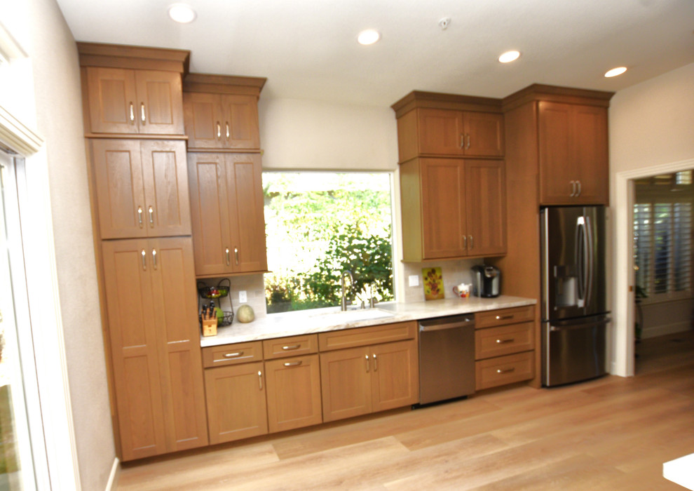 Large transitional u-shaped vinyl floor and brown floor kitchen photo with an undermount sink, shaker cabinets, medium tone wood cabinets, quartzite countertops, beige backsplash, porcelain backsplash, stainless steel appliances, an island and beige countertops