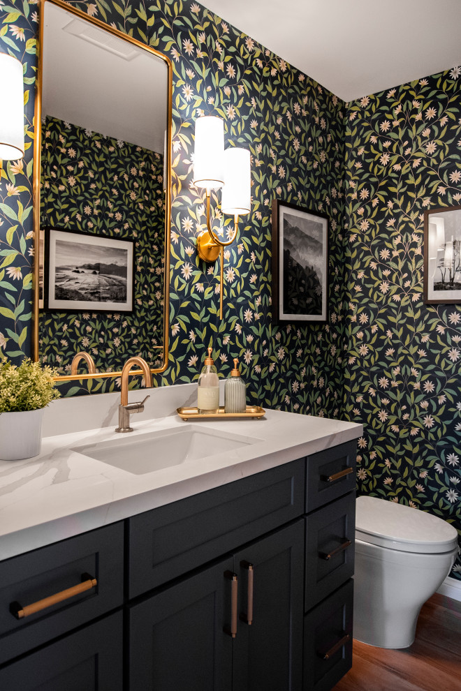 Example of a mid-sized transitional medium tone wood floor and wallpaper powder room design in San Francisco with shaker cabinets, blue cabinets, a one-piece toilet, an undermount sink, quartz countertops, white countertops and a built-in vanity