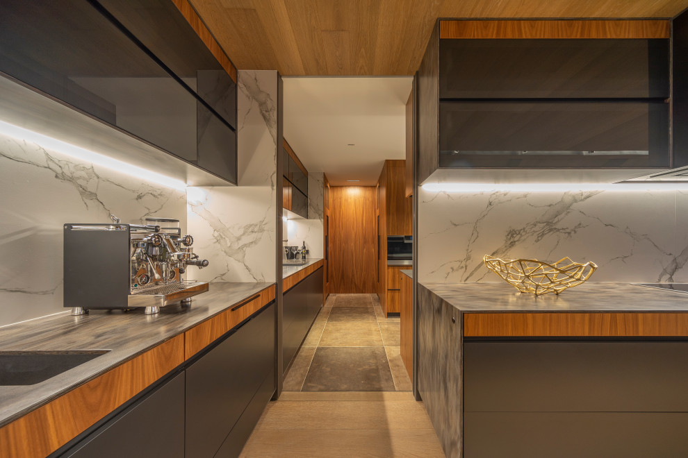 Expansive contemporary l-shaped open plan kitchen in Auckland with a submerged sink, flat-panel cabinets, black cabinets, composite countertops, black appliances, light hardwood flooring, an island, beige floors, multicoloured worktops, a vaulted ceiling, grey splashback and porcelain splashback.
