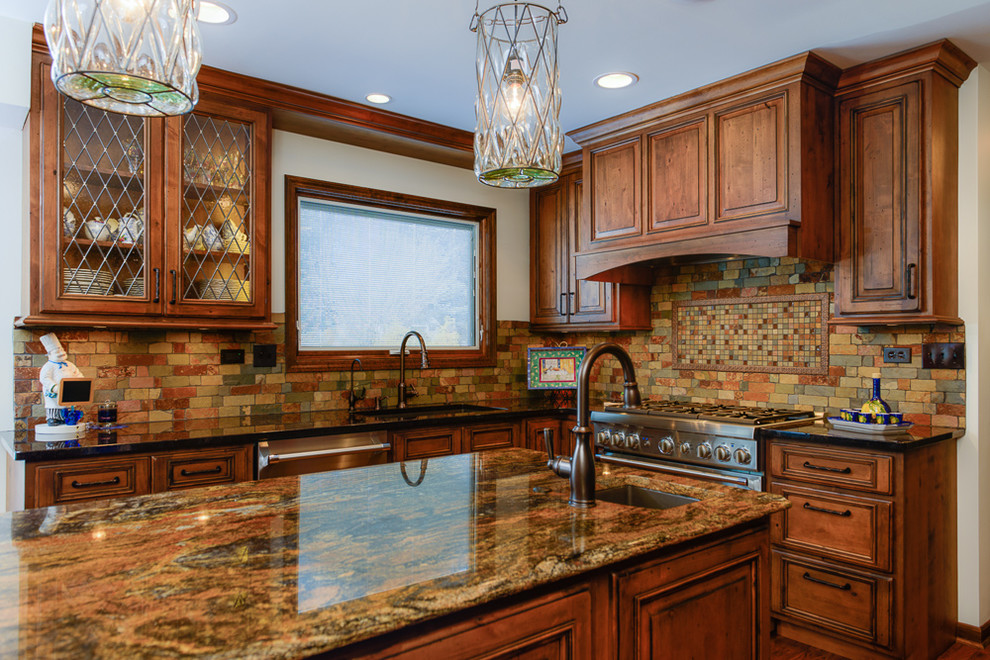 Example of a large mountain style kitchen design in Chicago with an undermount sink, raised-panel cabinets, granite countertops, stone tile backsplash, stainless steel appliances and an island