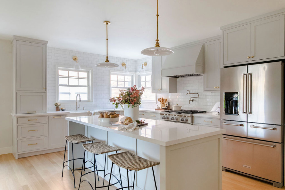 Design ideas for a large transitional l-shaped kitchen in Sacramento with a farmhouse sink, shaker cabinets, beige cabinets, white splashback, subway tile splashback, stainless steel appliances, light hardwood floors, with island, beige floor and white benchtop.