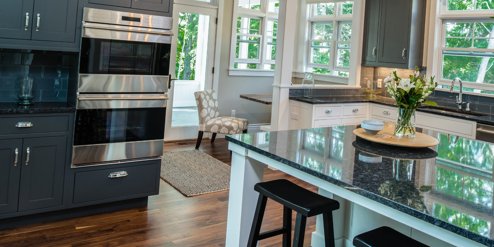 Example of a large transitional single-wall medium tone wood floor open concept kitchen design with an undermount sink, shaker cabinets, gray cabinets, granite countertops, gray backsplash, ceramic backsplash, stainless steel appliances and an island