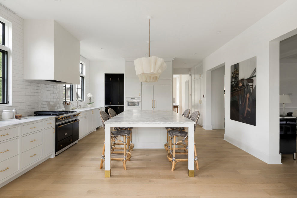 Inspiration for a transitional eat-in kitchen in Minneapolis with an undermount sink, beaded inset cabinets, white cabinets, marble benchtops, white splashback, ceramic splashback, black appliances, light hardwood floors, with island, beige floor and grey benchtop.