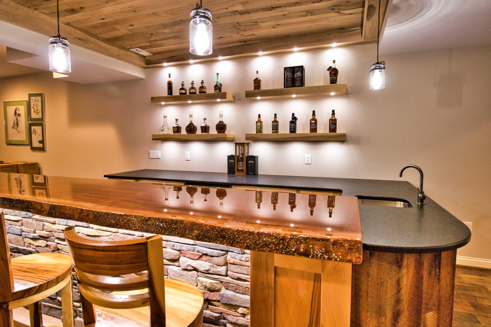 Inspiration for a large rustic u-shaped wet bar in Cincinnati with a submerged sink, shaker cabinets, light wood cabinets, granite worktops, laminate floors, brown floors and black worktops.