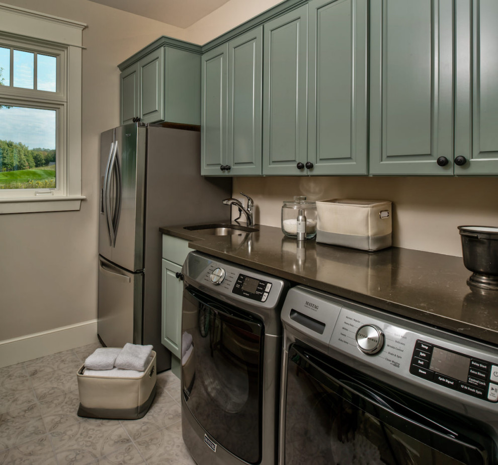 Design ideas for a mid-sized traditional single-wall dedicated laundry room in Other with an undermount sink, raised-panel cabinets, green cabinets, quartz benchtops, beige walls, ceramic floors, a side-by-side washer and dryer, beige floor and black benchtop.