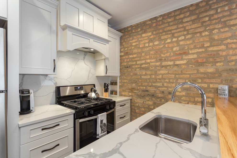 Mid-sized industrial galley open plan kitchen in Chicago with an undermount sink, flat-panel cabinets, white cabinets, wood benchtops, white splashback, marble splashback, stainless steel appliances, dark hardwood floors, with island and brown floor.