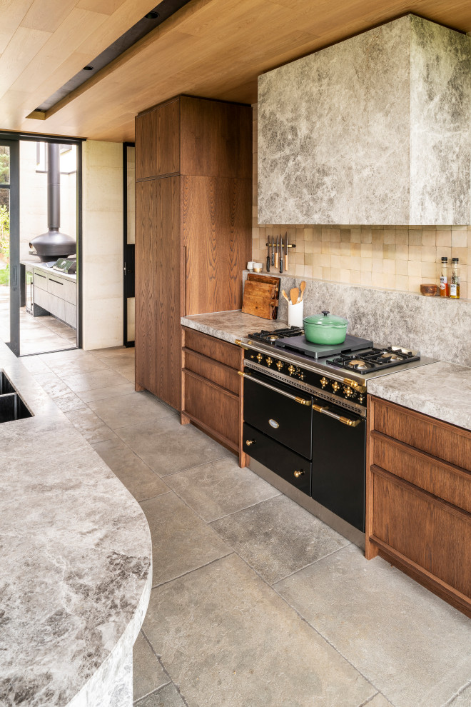 Design ideas for an expansive contemporary single-wall open plan kitchen in Melbourne with a double-bowl sink, flat-panel cabinets, medium wood cabinets, limestone benchtops, beige splashback, ceramic splashback, black appliances, with island, grey floor, grey benchtop and timber.