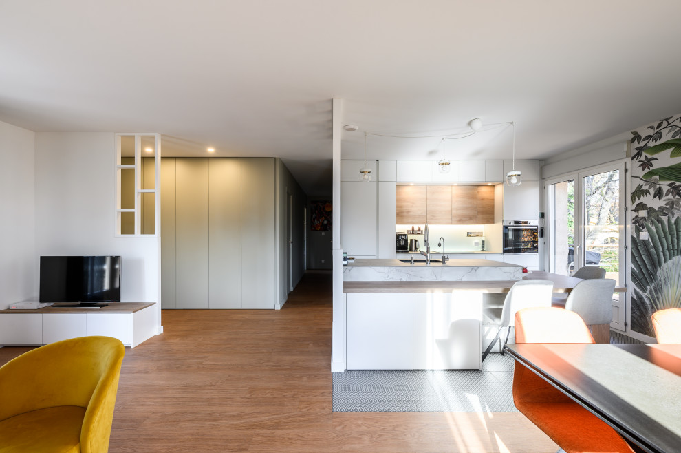 Modern inredning av ett mellanstort grå grått kök med öppen planlösning, med en integrerad diskho, luckor med profilerade fronter, vita skåp, laminatbänkskiva, vitt stänkskydd, integrerade vitvaror, cementgolv, en köksö och grönt golv
