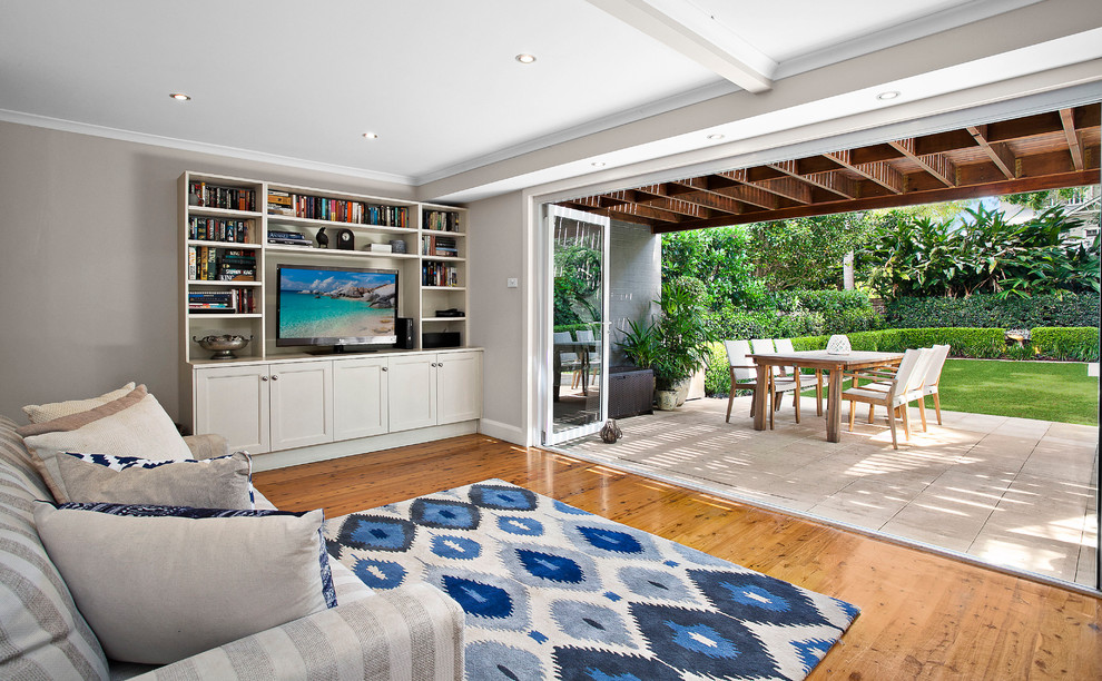 Inspiration for a small beach style open concept living room in Sydney with a library, beige walls, light hardwood floors and a built-in media wall.