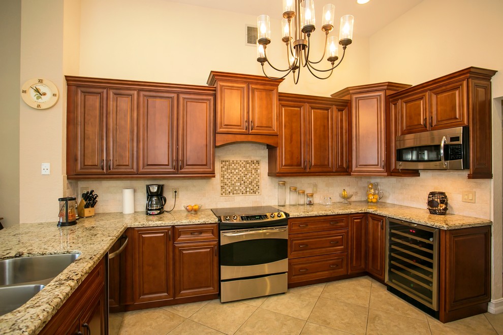 Example of a mid-sized transitional u-shaped porcelain tile eat-in kitchen design in Miami with an undermount sink, raised-panel cabinets, brown cabinets, granite countertops, beige backsplash, stone tile backsplash, stainless steel appliances, beige walls and a peninsula