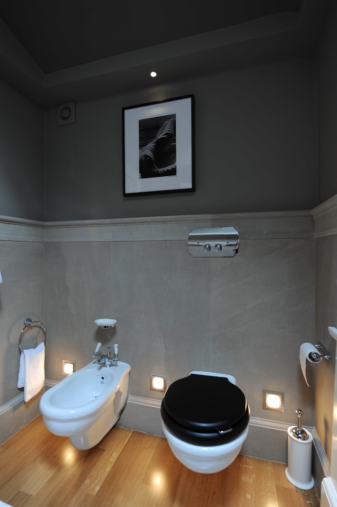 Foto på ett stort funkis toalett, med luckor med lamellpanel, vita skåp, en vägghängd toalettstol, grå kakel, stenhäll, grå väggar, målat trägolv, ett undermonterad handfat och marmorbänkskiva