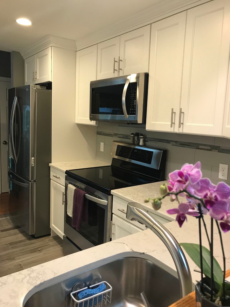 Inspiration for a mid-sized transitional l-shaped porcelain tile and gray floor open concept kitchen remodel in Boston with a single-bowl sink, flat-panel cabinets, white cabinets, quartz countertops, gray backsplash, subway tile backsplash, stainless steel appliances, an island and white countertops