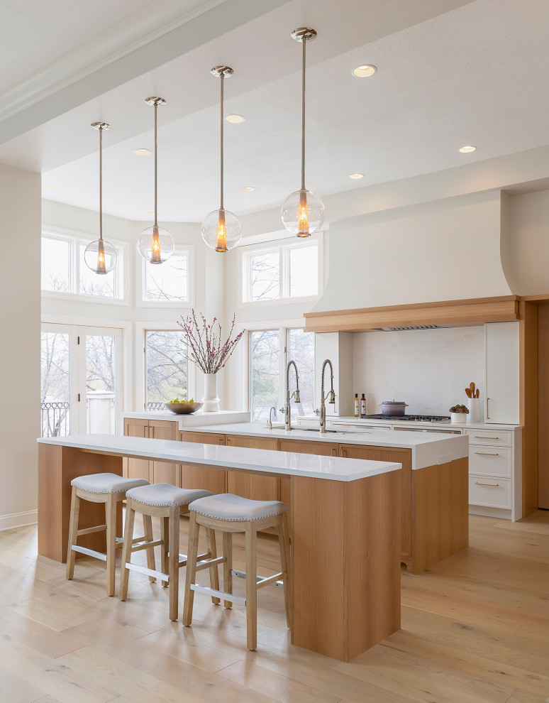 Exempel på ett stort klassiskt vit linjärt vitt kök med öppen planlösning, med en undermonterad diskho, släta luckor, skåp i ljust trä, bänkskiva i kvarts, vitt stänkskydd, rostfria vitvaror, ljust trägolv, flera köksöar och brunt golv