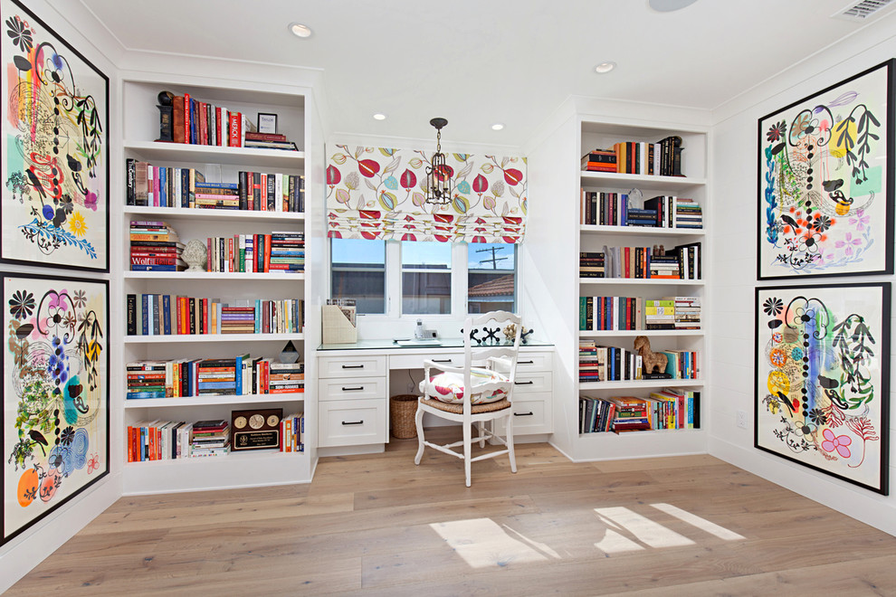 This is an example of a large transitional home office in Orange County with a library, white walls, medium hardwood floors and a built-in desk.