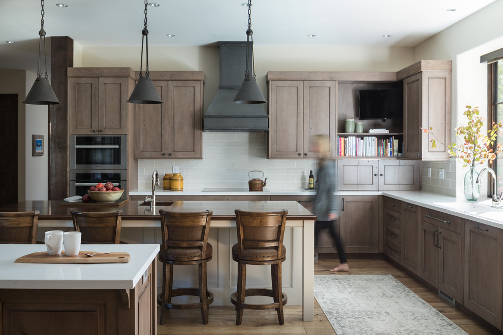 Inspiration for a country l-shaped kitchen in Other with a single-bowl sink, recessed-panel cabinets, brown cabinets, grey splashback, subway tile splashback, stainless steel appliances, medium hardwood floors, multiple islands and white benchtop.