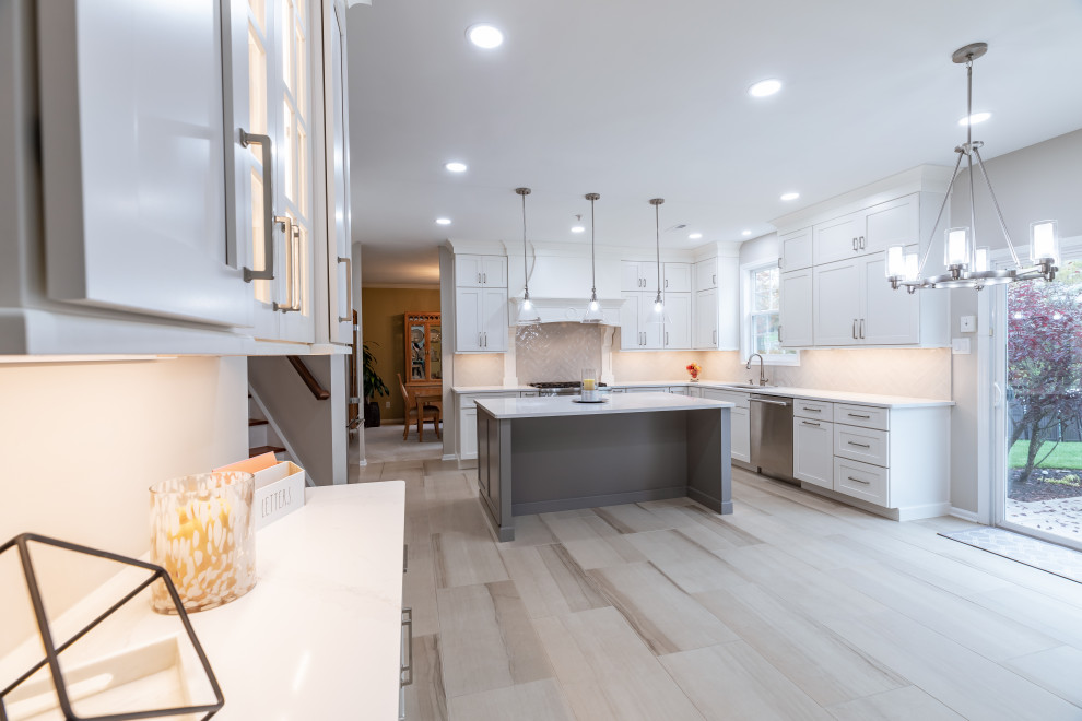 This is an example of a large contemporary l-shaped open plan kitchen in Philadelphia with a submerged sink, shaker cabinets, white cabinets, quartz worktops, beige splashback, ceramic splashback, stainless steel appliances, porcelain flooring, an island, beige floors and white worktops.