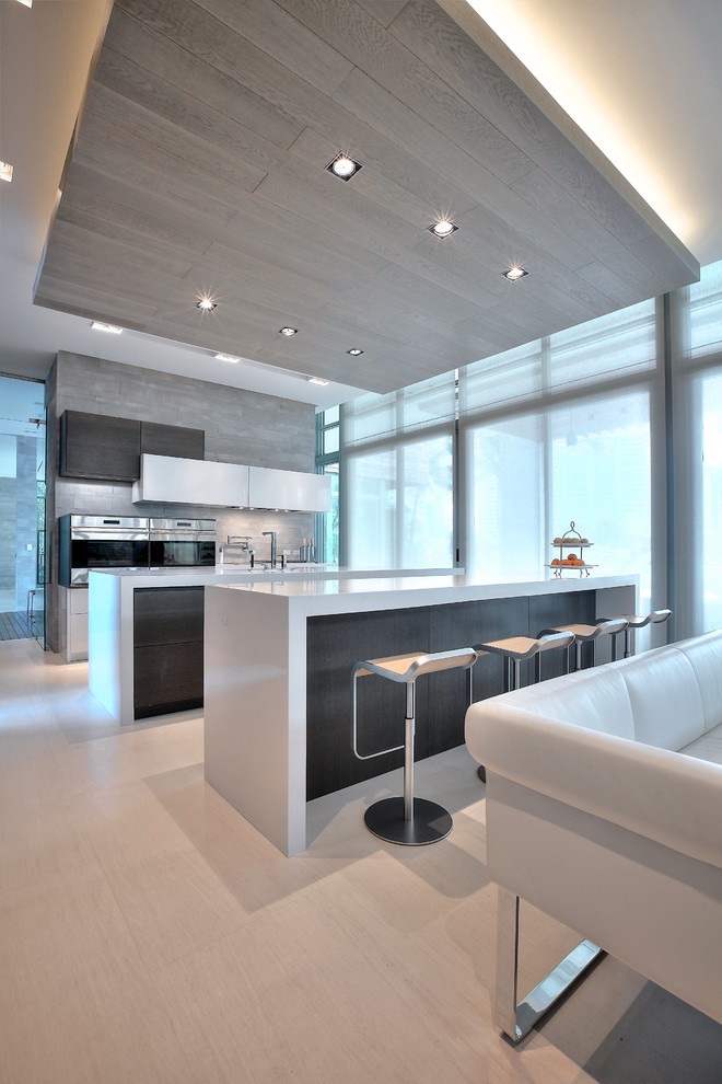 This is an example of a large modern galley eat-in kitchen in Miami with a double-bowl sink, flat-panel cabinets, white cabinets, quartz benchtops, grey splashback, ceramic splashback, stainless steel appliances, light hardwood floors and multiple islands.
