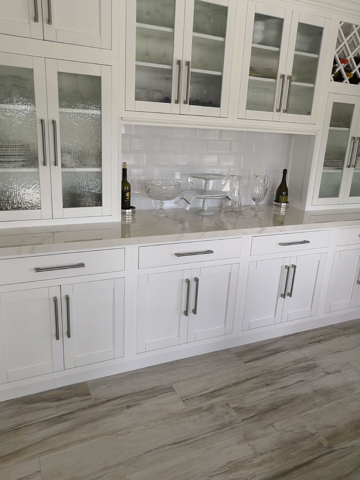 Mid-sized transitional u-shaped eat-in kitchen in Los Angeles with a farmhouse sink, recessed-panel cabinets, white cabinets, solid surface benchtops, white splashback, subway tile splashback, stainless steel appliances, porcelain floors, with island, grey floor and white benchtop.
