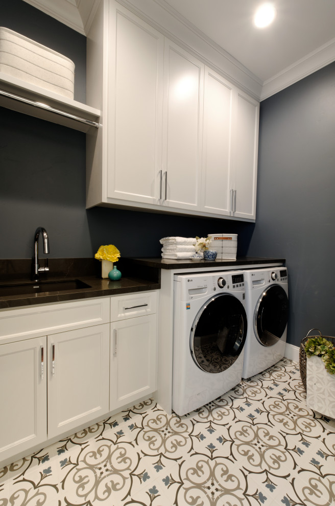 This is an example of a small contemporary galley dedicated laundry room in San Francisco with an undermount sink, shaker cabinets, grey cabinets, quartz benchtops, blue walls, porcelain floors, a side-by-side washer and dryer, white floor and black benchtop.