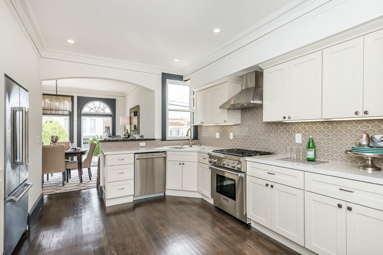 Mid-sized transitional u-shaped eat-in kitchen in San Francisco with a double-bowl sink, shaker cabinets, white cabinets, solid surface benchtops, beige splashback, ceramic splashback, stainless steel appliances, dark hardwood floors and a peninsula.