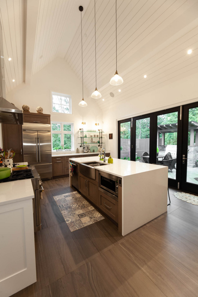 Large farmhouse u-shaped kitchen/diner in Vancouver with a belfast sink, shaker cabinets, grey cabinets, engineered stone countertops, white splashback, engineered quartz splashback, stainless steel appliances, porcelain flooring, an island, grey floors, white worktops and a vaulted ceiling.