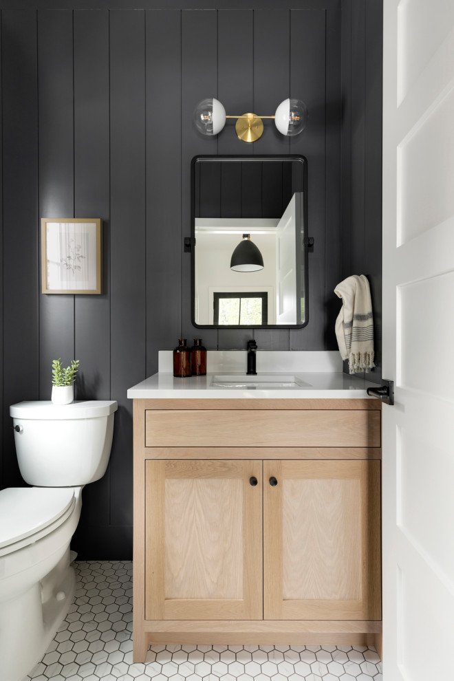 This is an example of a transitional powder room in Minneapolis with shaker cabinets, light wood cabinets, a two-piece toilet, black walls, mosaic tile floors, an undermount sink, white floor, white benchtops, a built-in vanity and planked wall panelling.