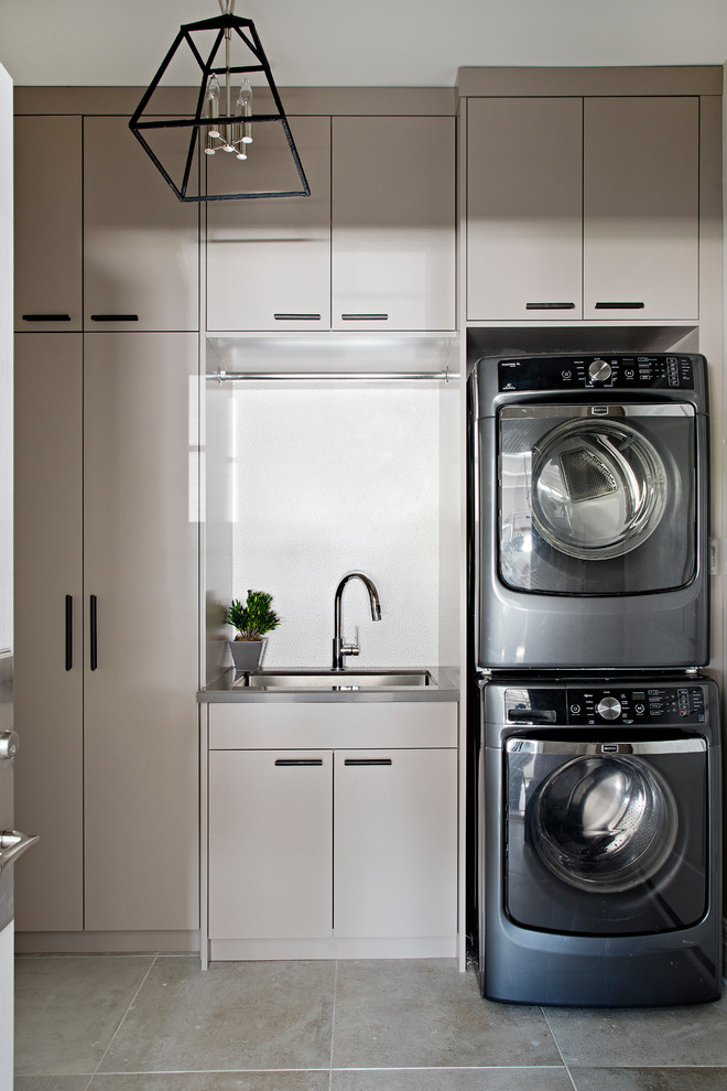 Photo of a small contemporary utility room in Toronto with an undermount sink, flat-panel cabinets, grey cabinets, quartz benchtops, grey walls, ceramic floors, a stacked washer and dryer, multi-coloured floor and grey benchtop.