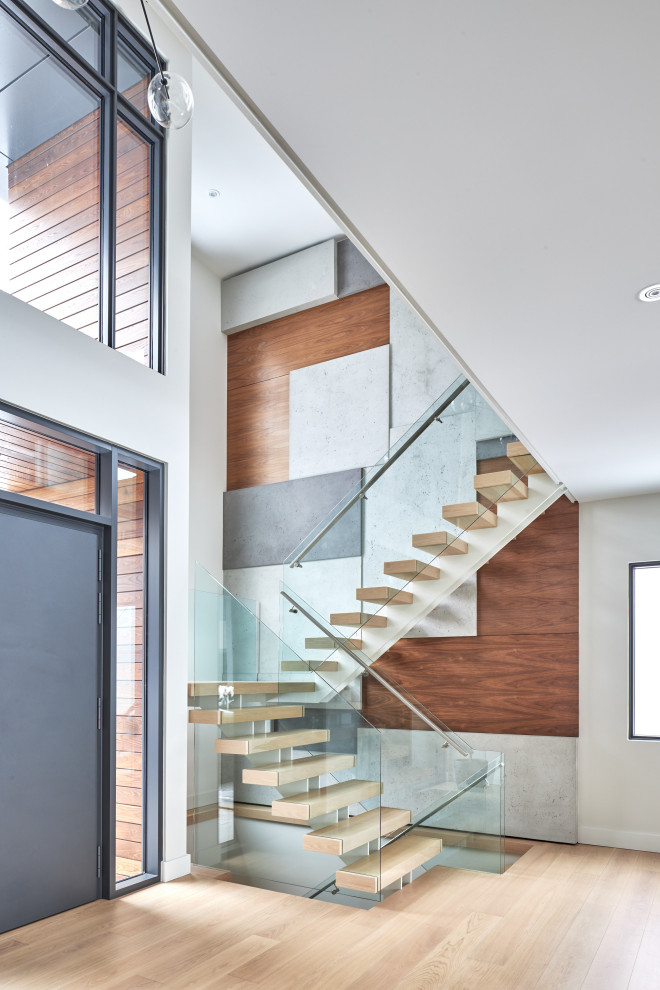 Large contemporary wood l-shaped glass railing staircase in Toronto with open risers and panelled walls.
