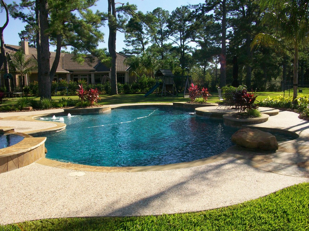 Mid-sized traditional backyard custom-shaped natural pool in Houston with concrete slab and a hot tub.