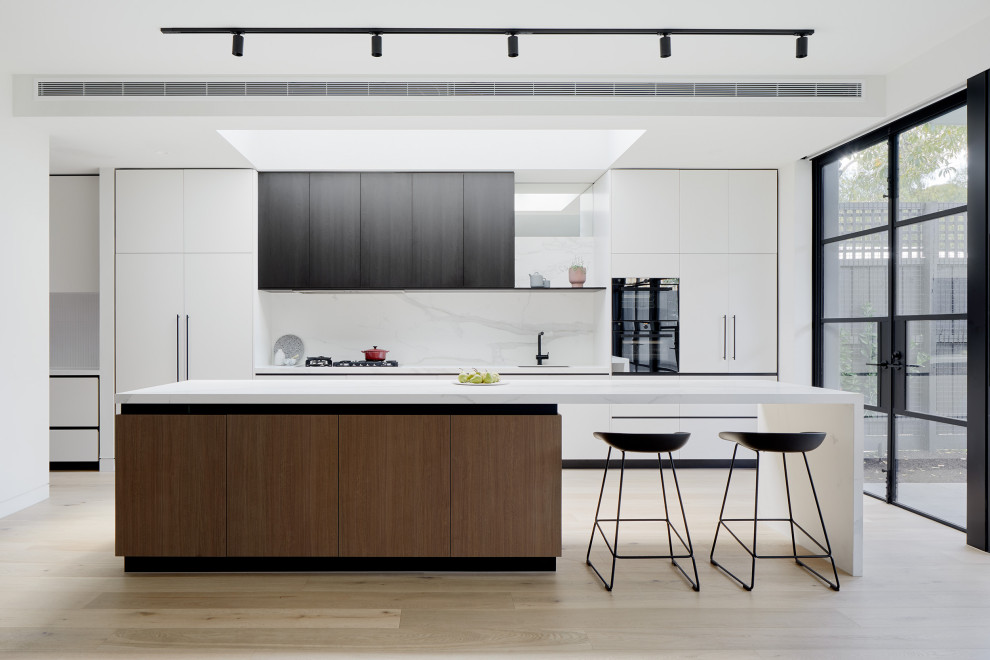 Inspiration for a large contemporary galley kitchen in Melbourne with an undermount sink, flat-panel cabinets, white cabinets, white splashback, black appliances, with island, beige floor and white benchtop.