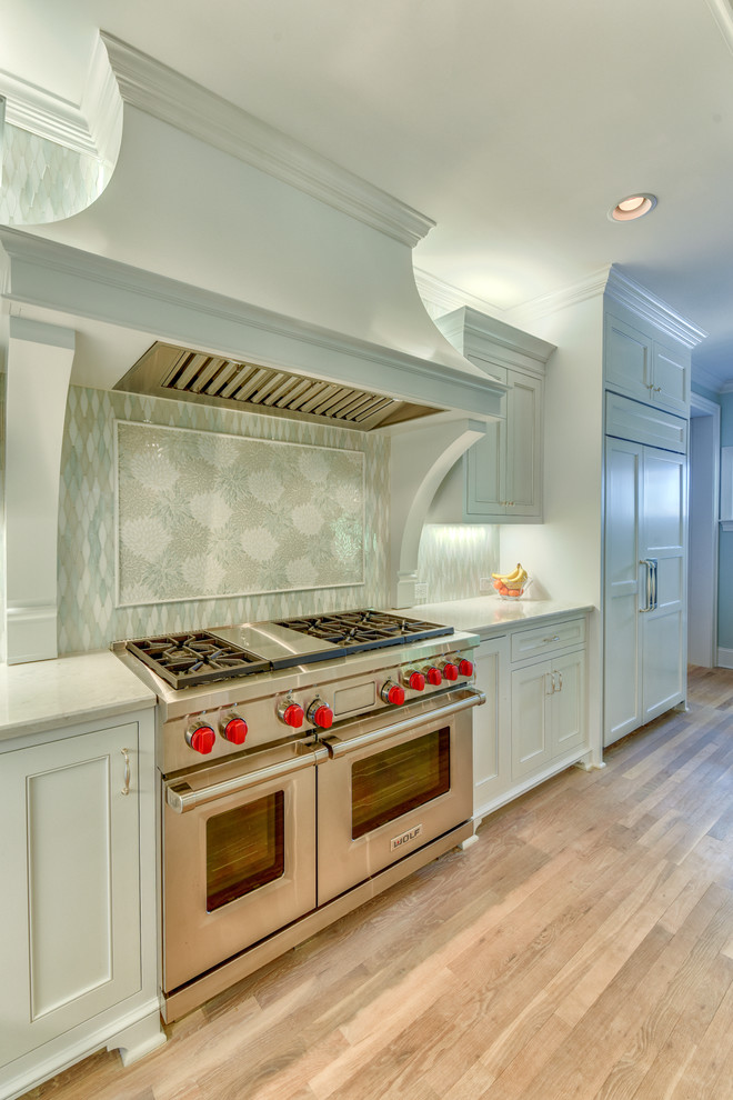 Photo of a large contemporary l-shaped eat-in kitchen in Charlotte with a farmhouse sink, recessed-panel cabinets, white cabinets, marble benchtops, white splashback, ceramic splashback, stainless steel appliances, light hardwood floors and with island.
