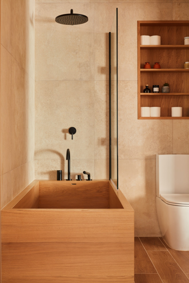 Стильный дизайн: главная ванная комната среднего размера в стиле модернизм с плоскими фасадами, черными фасадами, японской ванной, душем над ванной, унитазом-моноблоком, бежевой плиткой, керамогранитной плиткой, бежевыми стенами, полом из керамогранита, подвесной раковиной, бежевым полом, нишей, тумбой под одну раковину и подвесной тумбой - последний тренд