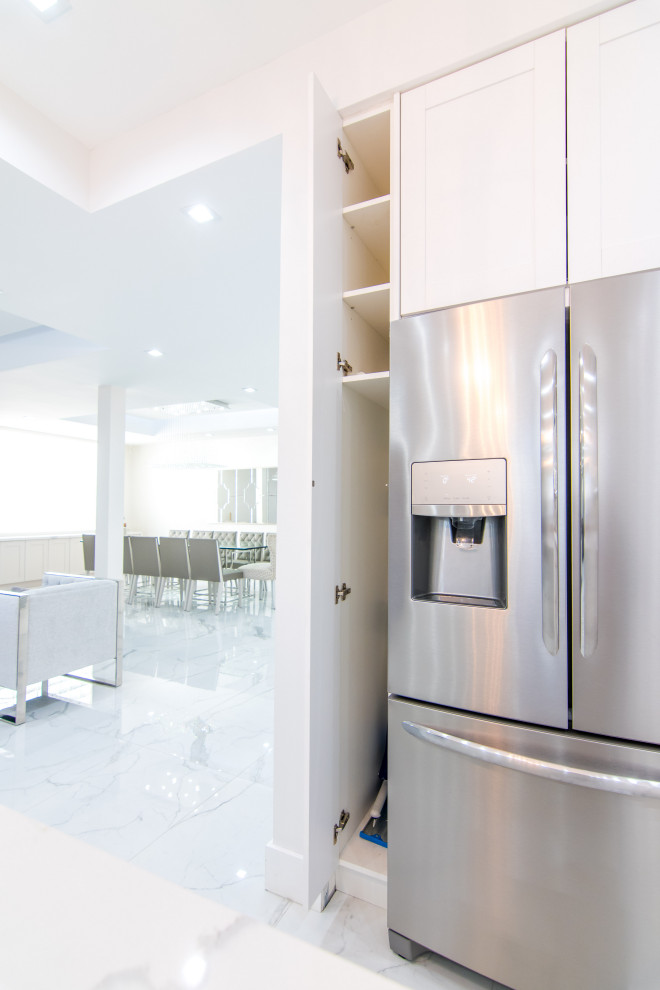 Large transitional l-shaped porcelain tile and white floor open concept kitchen photo in Miami with an undermount sink, shaker cabinets, white cabinets, quartz countertops, white backsplash, porcelain backsplash, stainless steel appliances, an island and white countertops