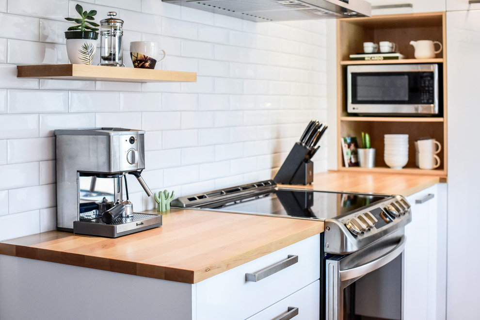 Small scandinavian l-shaped separate kitchen in Montreal with an undermount sink, flat-panel cabinets, white cabinets, quartzite benchtops, white splashback, ceramic splashback, stainless steel appliances, medium hardwood floors, with island and orange floor.