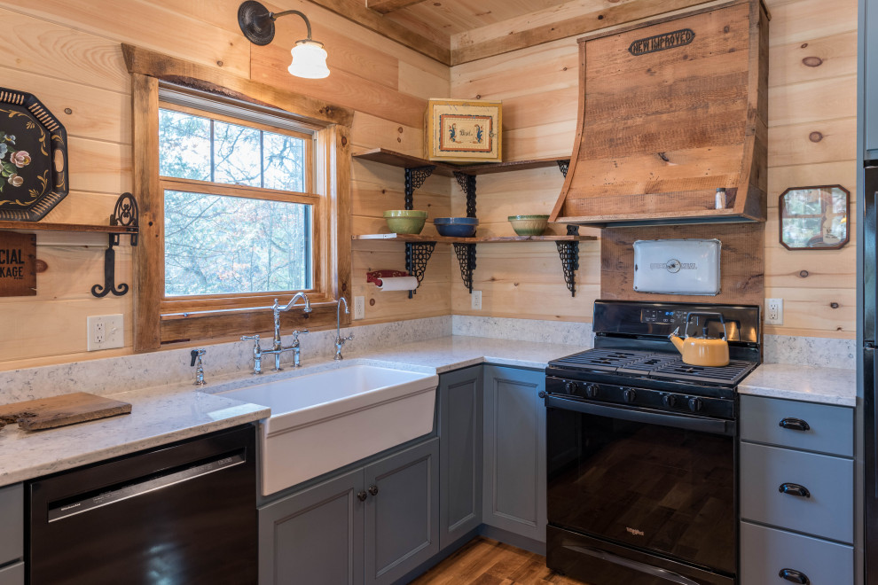 This is an example of a small country kitchen in Minneapolis with a farmhouse sink, blue cabinets, quartz benchtops, black appliances, medium hardwood floors, brown floor, white benchtop and recessed-panel cabinets.