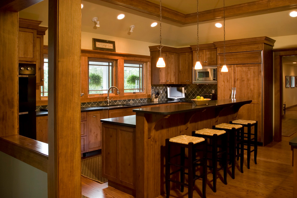 Inspiration for a mid-sized country l-shaped eat-in kitchen in Boston with an undermount sink, medium wood cabinets, stone tile splashback, black appliances, medium hardwood floors, with island and recessed-panel cabinets.