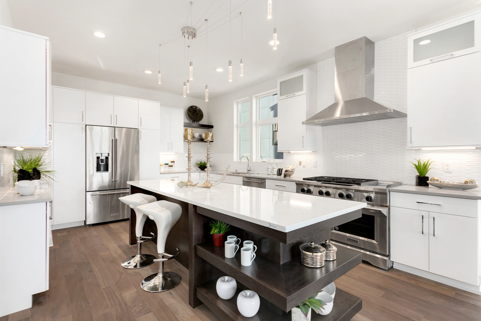 Photo of a large contemporary u-shaped open plan kitchen in Seattle with flat-panel cabinets, white cabinets, white splashback, matchstick tile splashback, stainless steel appliances, medium hardwood floors, with island, brown floor and white benchtop.