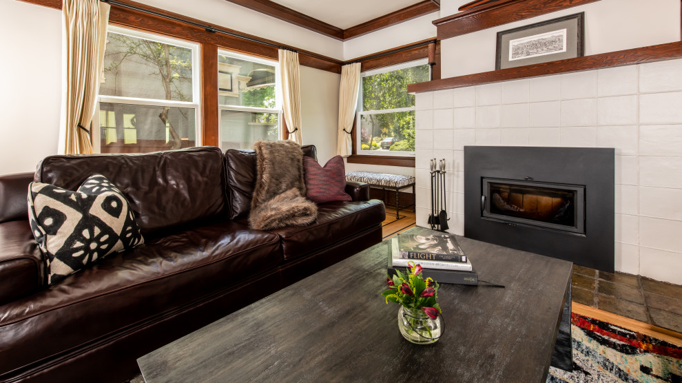 Exemple d'un grand salon craftsman fermé avec une salle de réception, un mur blanc, un sol en bois brun, une cheminée standard, un manteau de cheminée en carrelage, aucun téléviseur et poutres apparentes.