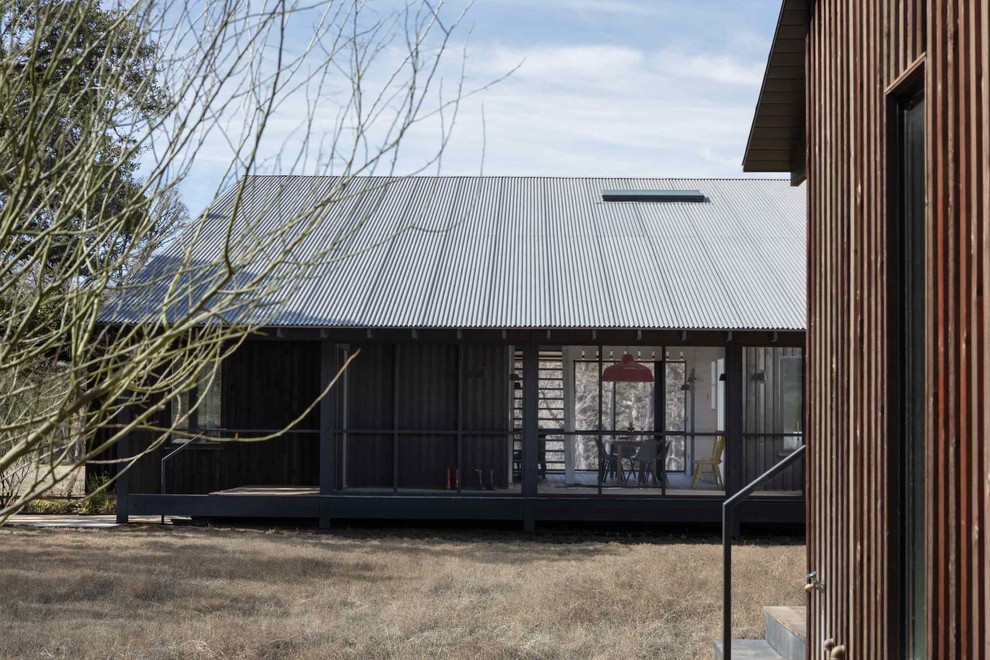 Country two-storey black house exterior in Austin with wood siding, a shed roof and a metal roof.