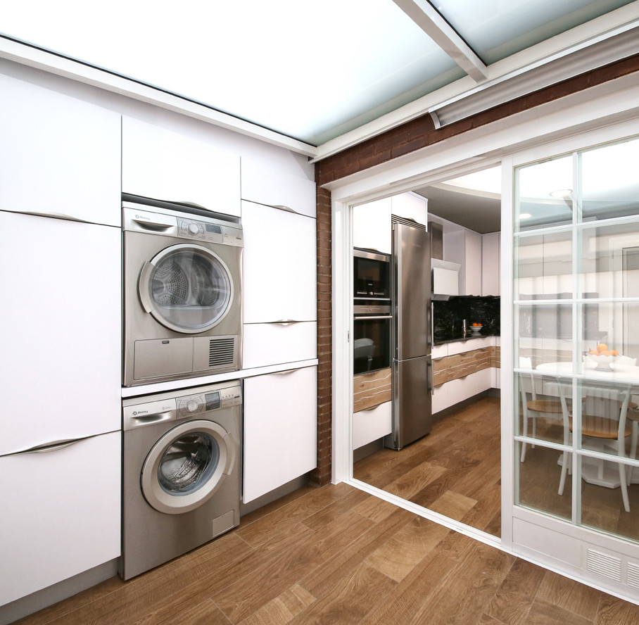 Mid-sized contemporary single-wall dedicated laundry room in Other with flat-panel cabinets, white cabinets, medium hardwood floors and a stacked washer and dryer.