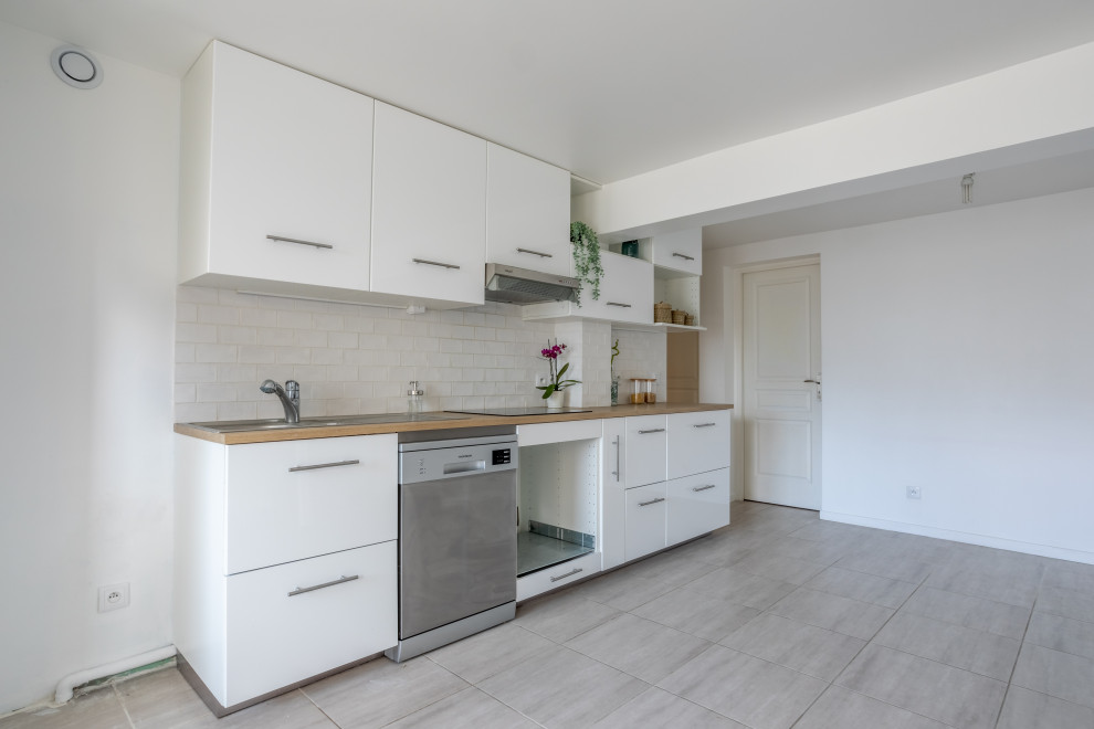 Design ideas for a mid-sized contemporary single-wall open plan kitchen in Paris with a single-bowl sink, flat-panel cabinets, white cabinets, laminate benchtops, white splashback, ceramic splashback, stainless steel appliances, ceramic floors and grey floor.