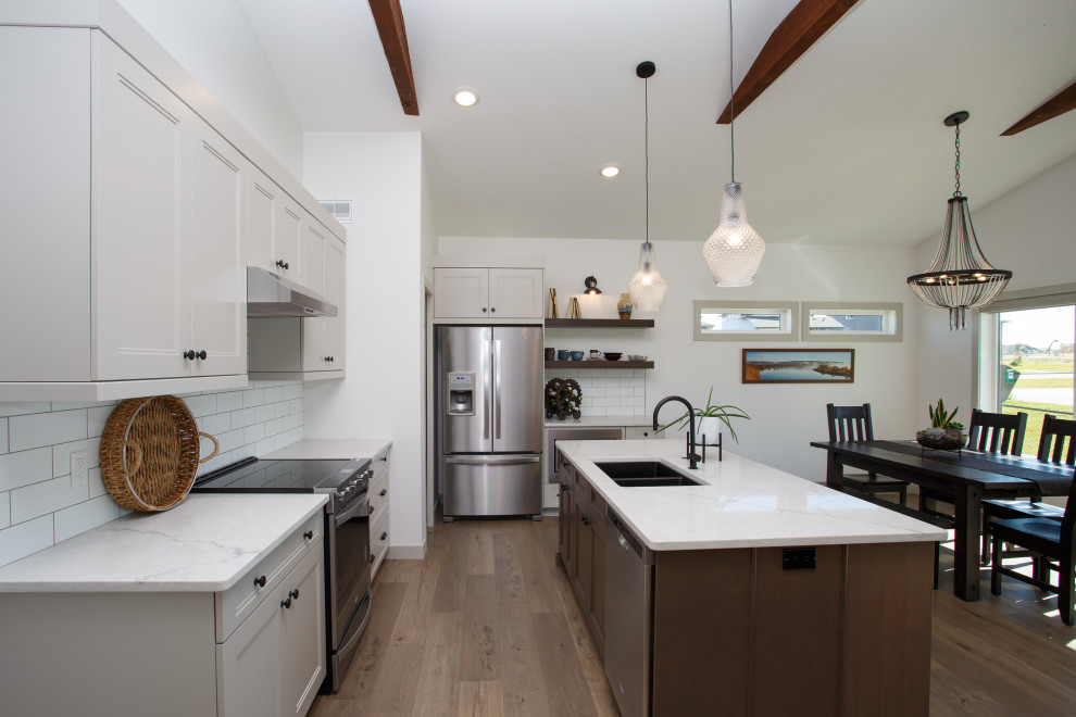 Photo of a mid-sized beach style l-shaped open plan kitchen in Calgary with an undermount sink, recessed-panel cabinets, grey cabinets, quartz benchtops, white splashback, subway tile splashback, stainless steel appliances, vinyl floors, with island, brown floor, white benchtop and exposed beam.